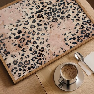May include: A framed print with a pink and brown abstract leopard print pattern. The print is in a wooden frame and is sitting on a wooden table.