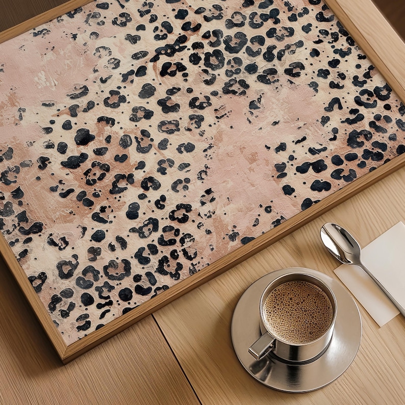 May include: A framed print with a pink and brown abstract leopard print pattern. The print is in a wooden frame and is sitting on a wooden table.