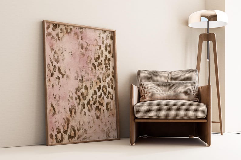 May include: A framed print of a pink and brown abstract leopard print design. The print is hanging on a white wall next to a brown armchair with a checkered pattern.