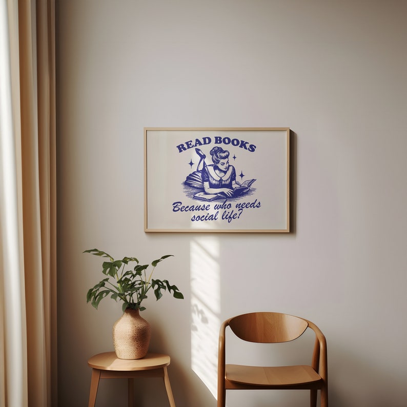 May include: A framed print featuring a blue ink illustration of a woman reading a book, with the text "READ BOOKS Because who needs social life?" The print is set within a light wood frame.