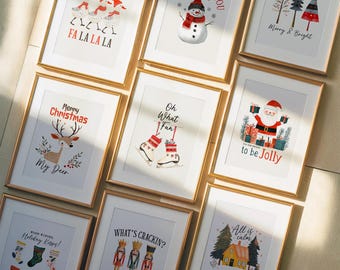 Può includere: Una collezione di stampe artistiche natalizie incorniciate con cornici dorate. Le stampe presentano illustrazioni festive di pupazzi di neve, renne, Babbo Natale e schiaccianoci, insieme a frasi di festa come "Merry Christmas" e "What's Crackin?"