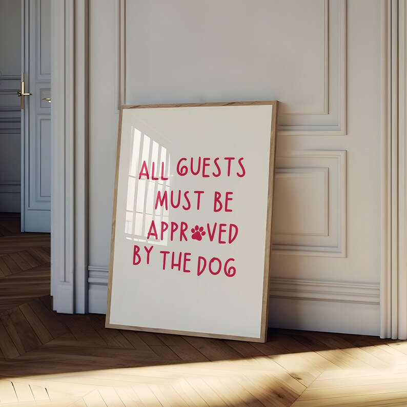 Puede incluir: Una impresi&oacute;n enmarcada con el texto "ALL GUESTS MUST BE APPROVED BY THE DOG" en letras rosas con una huella de pata en la palabra "APPROVED".