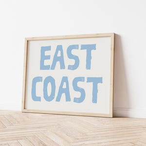 May include: A framed print with the text "EAST COAST" in a light blue color on a white background.