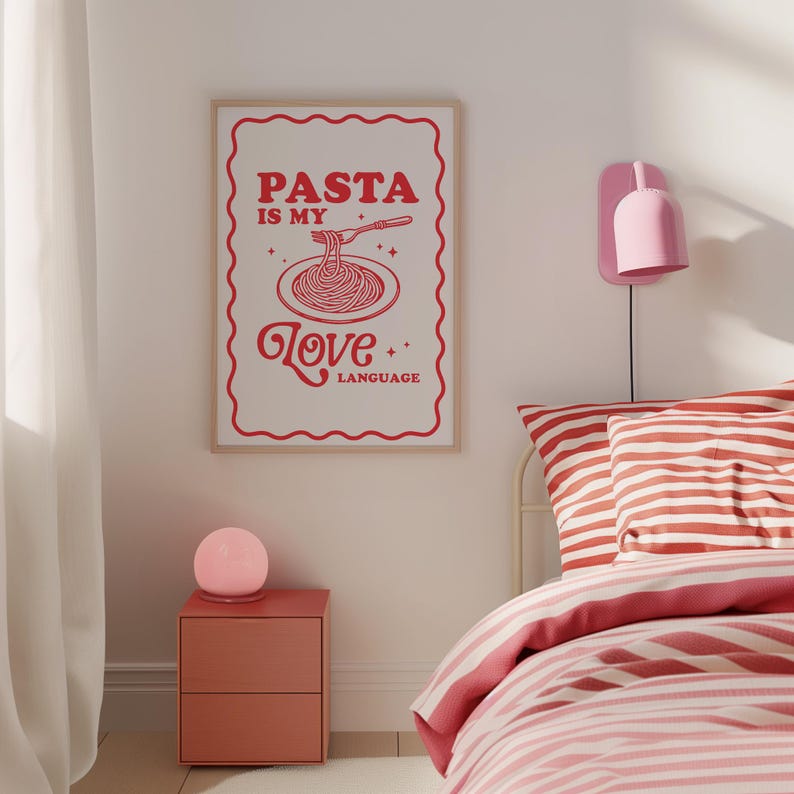 May include: A white poster with red text that reads "PASTA IS MY LOVE LANGUAGE" with a stylized illustration of a plate of spaghetti and a fork. The poster is hanging on a white wall above a red nightstand with a pink lamp.