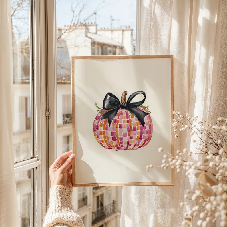 May include: A watercolor painting of a pink and white checkered pumpkin with a black bow. The pumpkin is surrounded by a white background.