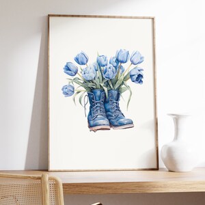 K&ouml;nnte beinhalten: Ein gerahmtes Aquarellbild von blauen Tulpen in einem Paar blauer Stiefel. Die Stiefel sind mit Schn&uuml;rsenkeln gebunden und die Tulpen sind zu einem Strau&szlig; angeordnet.