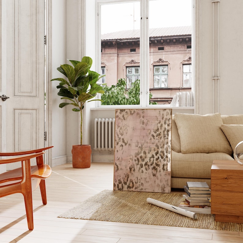 May include: A living room interior with a beige sofa, a wooden coffee table, a brown plant in a terracotta pot, and a large framed print of a pink and brown leopard print design.
