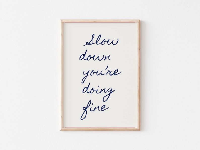 May include: A framed print with the text "Slow down you're doing fine" written in blue cursive script on a white background.