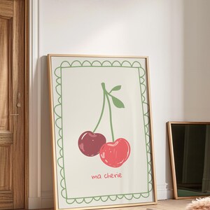 May include: A framed print with a green border featuring a drawing of two red cherries with a green stem and leaves. The text "ma ch&eacute;rie" is written below the cherries.