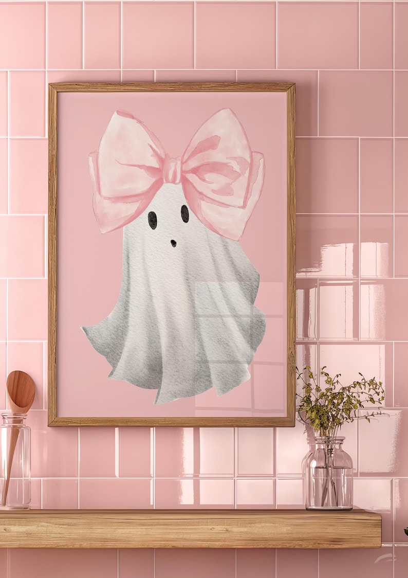 Pu&ograve; includere: Una stampa incorniciata di un fantasma bianco con un fiocco rosa su uno sfondo rosa.