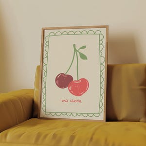 May include: A framed print with a white background and a green border. The print features a drawing of two red cherries on a stem with green leaves. The text "ma ch&eacute;rie" is written below the cherries.