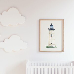 May include: A watercolor painting of a white lighthouse with a black roof and a blue window. The lighthouse is surrounded by green grass and is set against a white background. The painting is framed in a light wood frame.