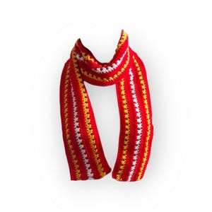 May include: A handmade crochet scarf in red, with vertical stripes of white and yellow. The scarf is displayed against a white background. The scarf is a winter accessory.