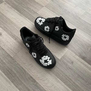 May include: A pair of black sneakers with white floral designs. The sneakers have a white sole and laces.
