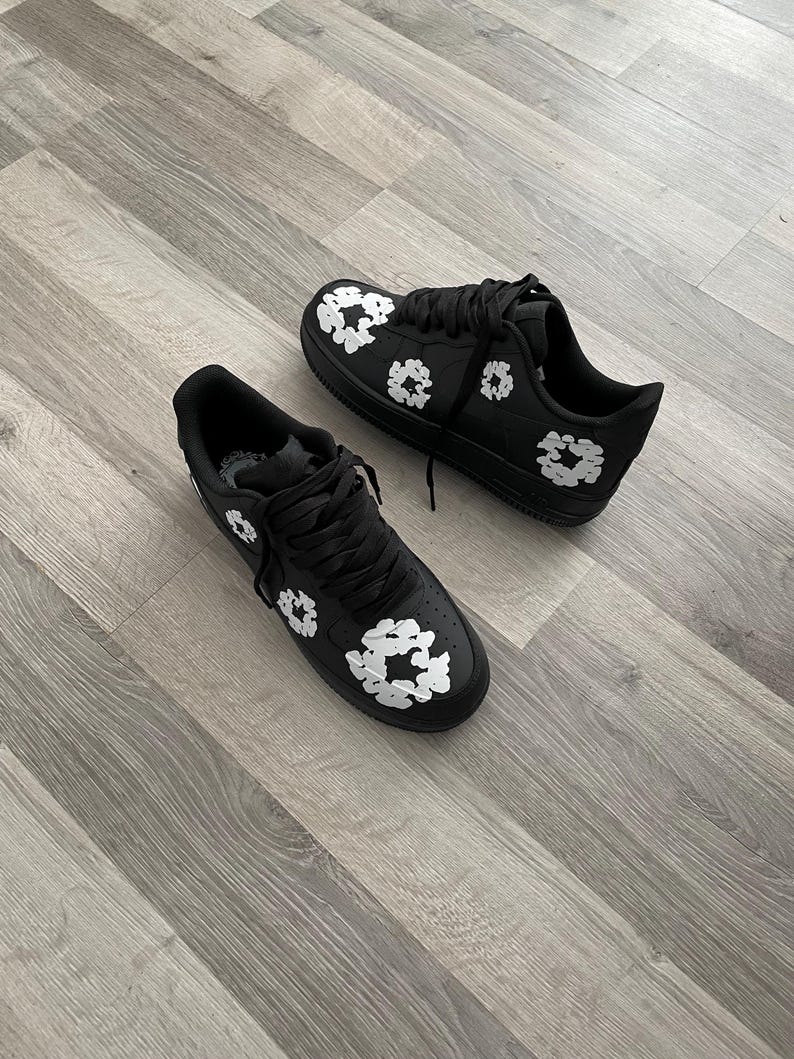 May include: A pair of black sneakers with white floral designs. The sneakers have a white sole and laces.