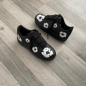 May include: A pair of black sneakers with white floral designs. The sneakers have a white sole and laces.