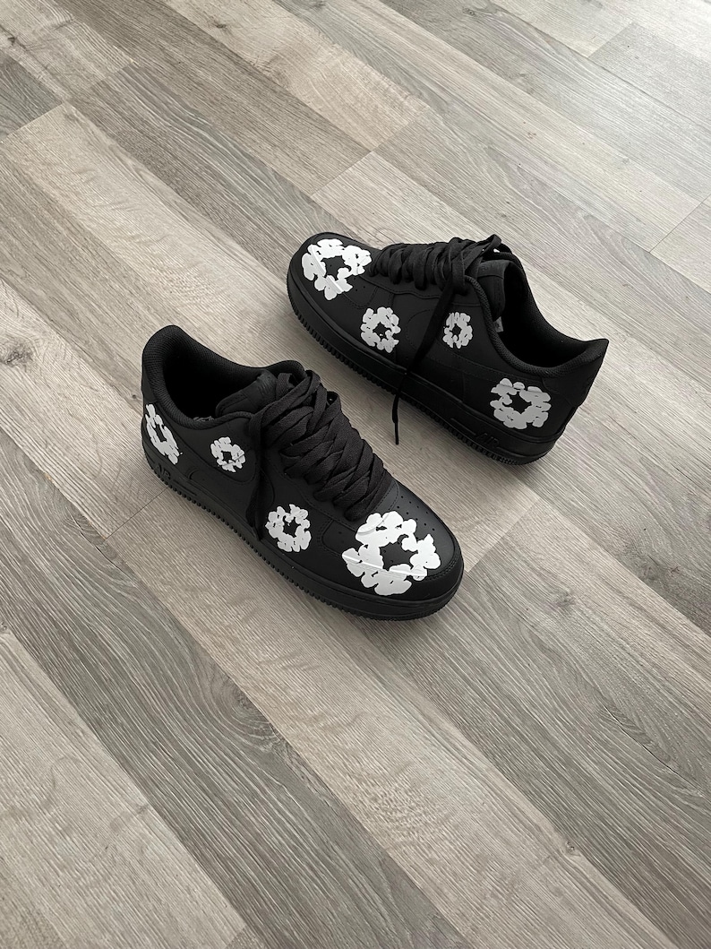 May include: A pair of black sneakers with white floral designs. The sneakers have a white sole and laces.