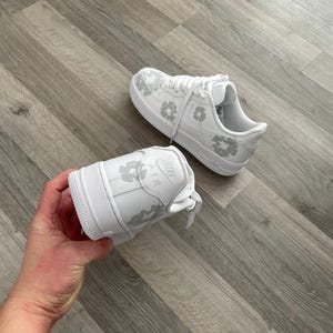 May include: White leather sneakers with a grey floral pattern. The sneakers have a white sole and a white lace.