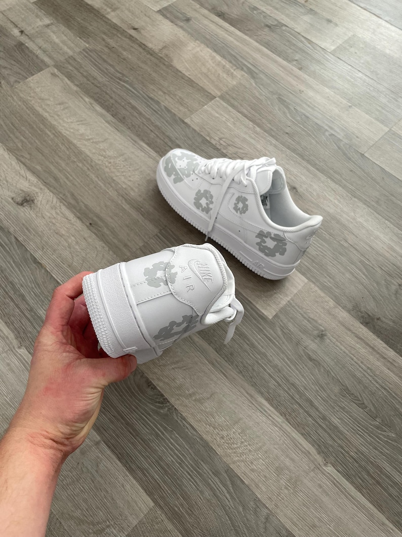 May include: White leather sneakers with a grey floral pattern. The sneakers have a white sole and a white lace.