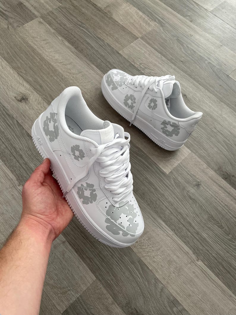 May include: White leather sneakers with a grey leopard print design. The sneakers have white laces and a white sole.
