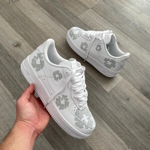 May include: White leather sneakers with a gray floral pattern. The sneakers have a white sole and laces.