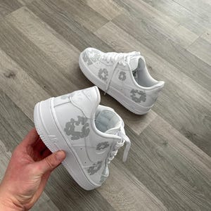 May include: White leather sneakers with a grey leopard print design. The sneakers have a white sole and laces.