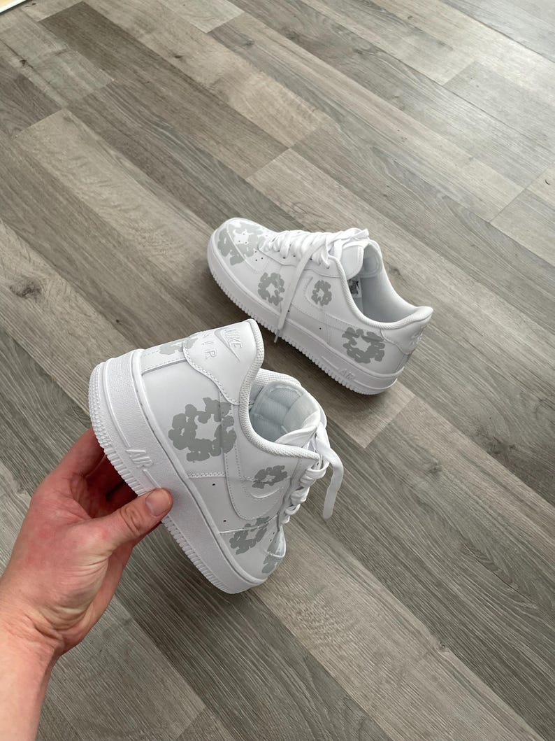 May include: White leather sneakers with a grey leopard print design. The sneakers have a white sole and laces.