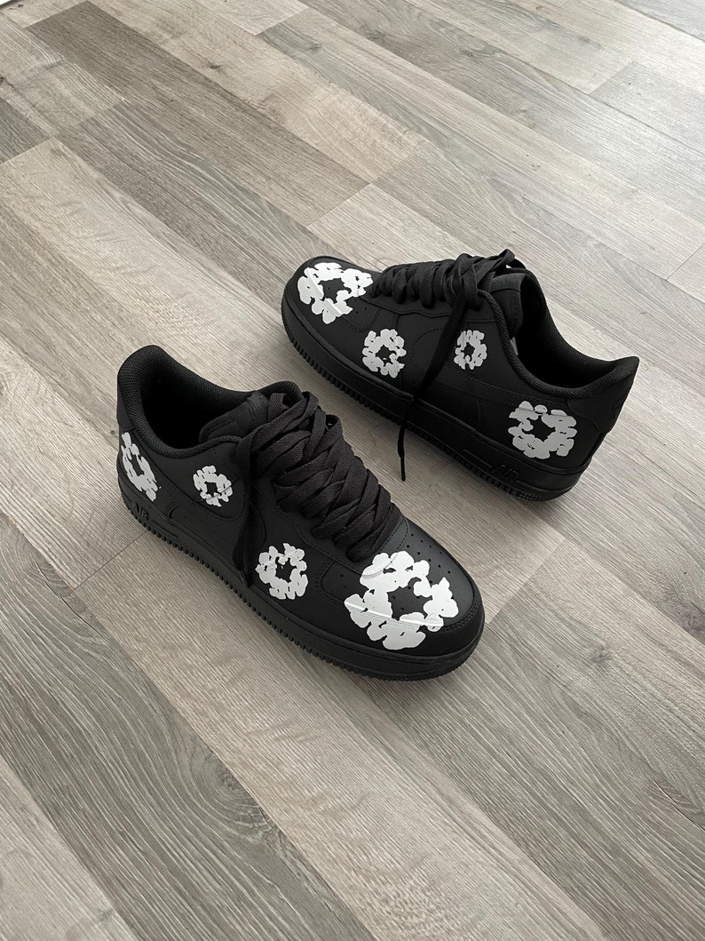 May include: A pair of black sneakers with white floral designs. The sneakers have black laces and a white swoosh logo on the side.