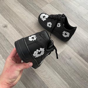 May include: Black leather sneakers with white floral print. The sneakers have a white "Nike Air" logo on the side.