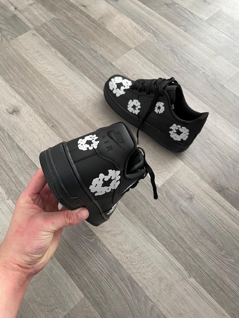 May include: Black leather sneakers with white floral print. The sneakers have a white "Nike Air" logo on the side.