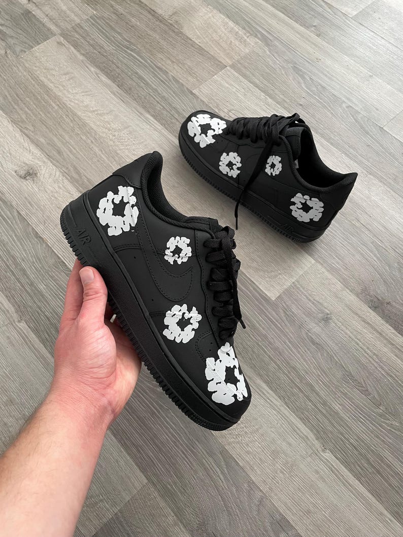 May include: Black leather sneakers with white floral designs. The sneakers have a white swoosh logo on the side and the word "AIR" on the back.