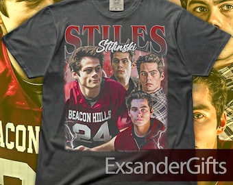 May include: Dark gray t-shirt featuring a collage of images of a person, with the name "Stiles Stilinski" in red and white text. The shirt also displays "Beacon Hills 24" in red and white.