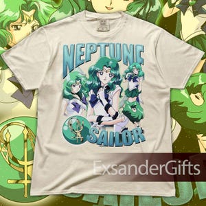 May include: Cream-colored t-shirt featuring a graphic of the character Sailor Neptune from the anime series Sailor Moon. The design includes the text "NEPTUNE SAILOR" in blue, along with multiple illustrations of the character. The shirt has a Comfort Colors tag.