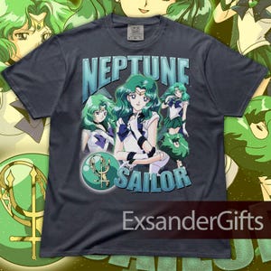 May include: Dark gray t-shirt featuring the words "NEPTUNE SAILOR" with an illustration of a character with green hair and a sailor uniform. The shirt has a vintage, distressed look, with the text and image in shades of blue and green.