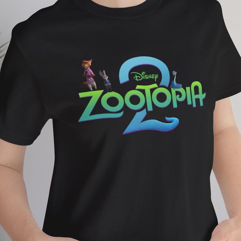Puede incluir: Camiseta negra con el logo de la pel&iacute;cula de Disney "Zootopia 2". El dise&ntilde;o incluye el t&iacute;tulo de la pel&iacute;cula en verde y azul, con el logotipo de Disney encima. La camiseta tambi&eacute;n muestra los personajes Nick Wilde y Judy Hopps.