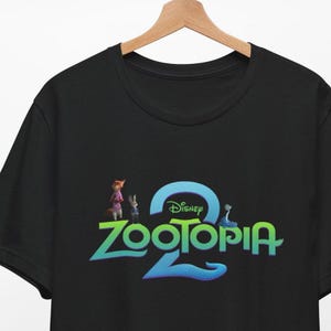 Puede incluir: Camiseta negra de cuello redondo con el logotipo de la pel&iacute;cula de Disney "Zootopia 2". El dise&ntilde;o incluye el t&iacute;tulo de la pel&iacute;cula en verde y azul, con el logotipo de Disney encima. La camiseta tambi&eacute;n presenta im&aacute;genes de los personajes.