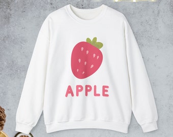 Puede incluir: Sudadera blanca con un gráfico de fresa rosa y la palabra "APPLE" en letras rosas.