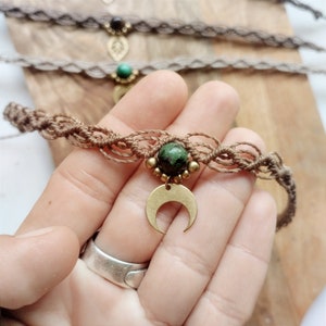 Puede incluir: Un tobillo de macramé marrón con una piedra verde y un dije de media luna.