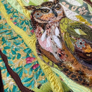 Close-up of the owl showing detailed fabric feathers, expressive eyes, floral accents, and layered textile textures.