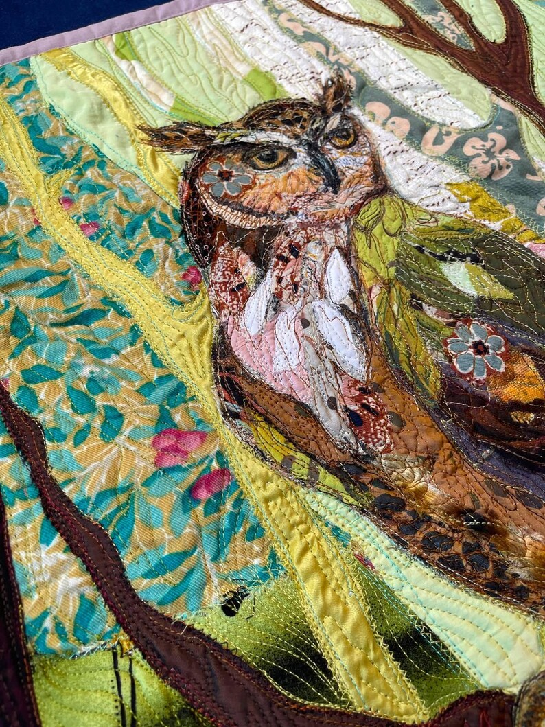 Close-up of the owl showing detailed fabric feathers, expressive eyes, floral accents, and layered textile textures.