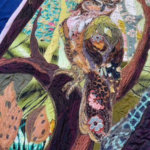 Close-up of the owl showing detailed fabric feathers, expressive eyes, floral accents, and layered textile textures.