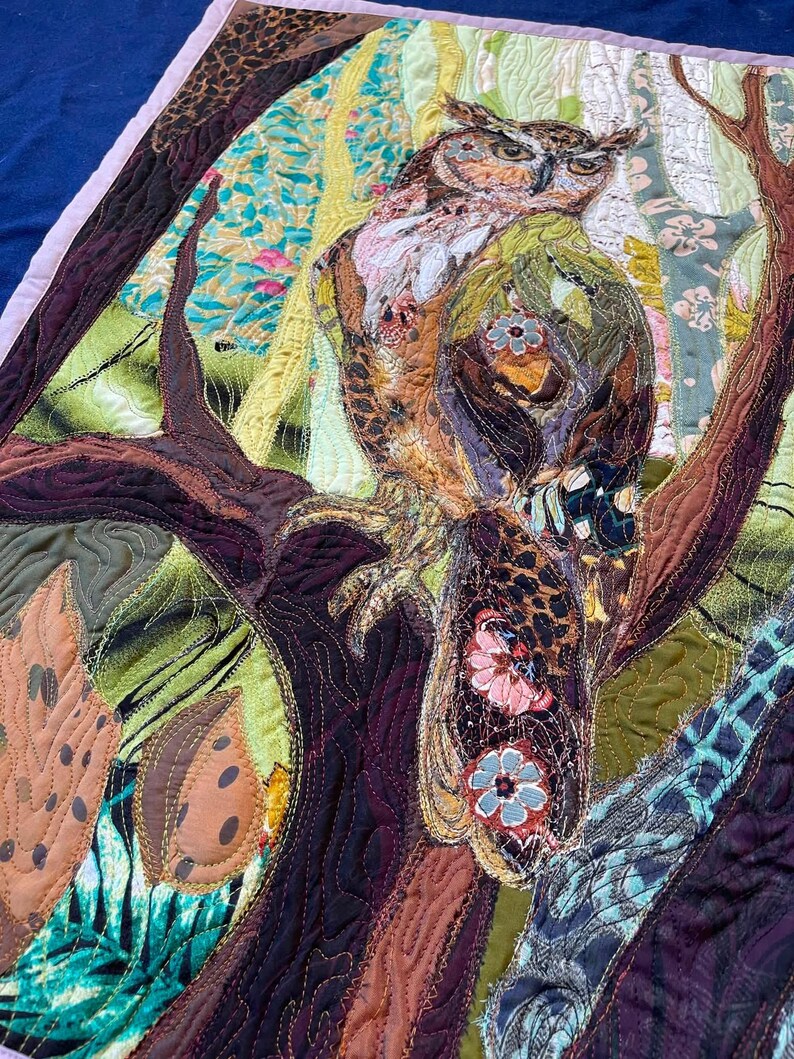 Close-up of the owl showing detailed fabric feathers, expressive eyes, floral accents, and layered textile textures.