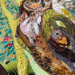 Close-up of the owl showing detailed fabric feathers, expressive eyes, floral accents, and layered textile textures.