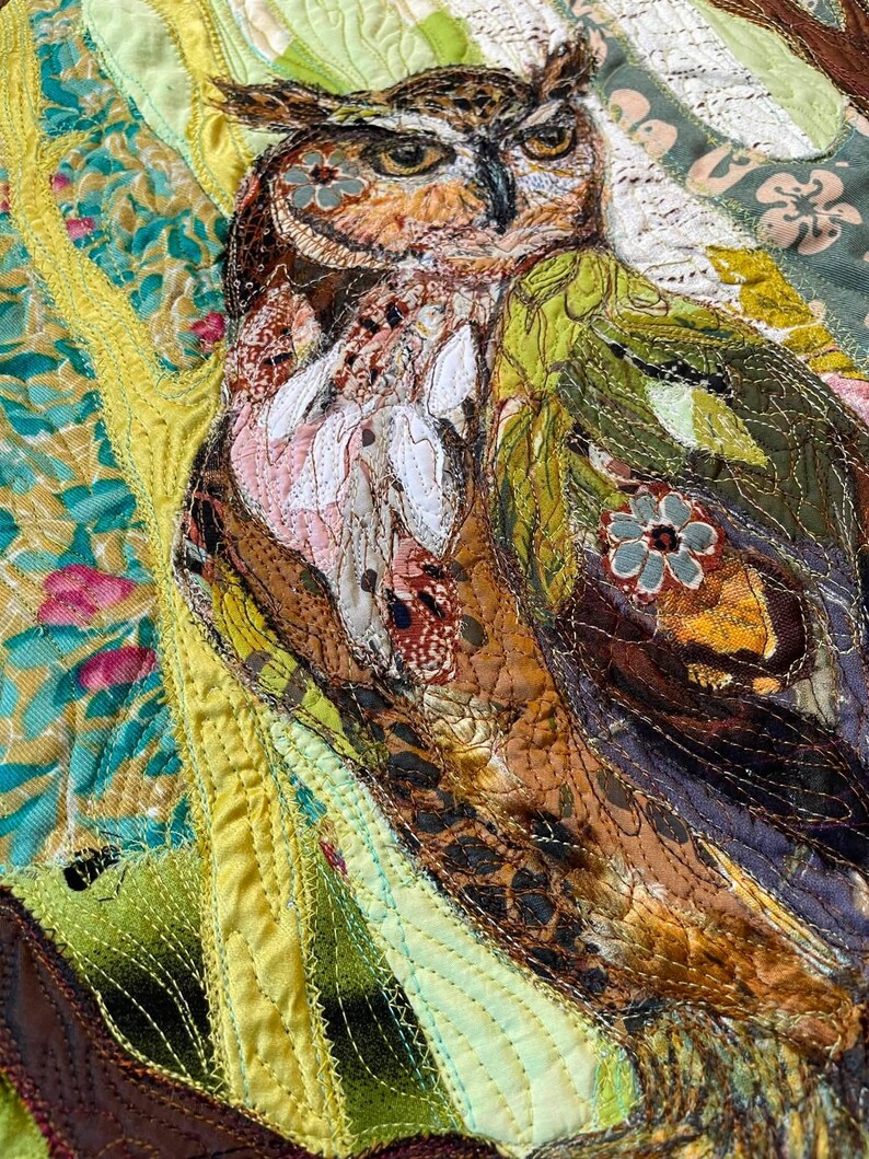 Close-up of the owl showing detailed fabric feathers, expressive eyes, floral accents, and layered textile textures.