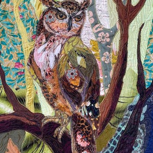 Close-up of the owl showing detailed fabric feathers, expressive eyes, floral accents, and layered textile textures.