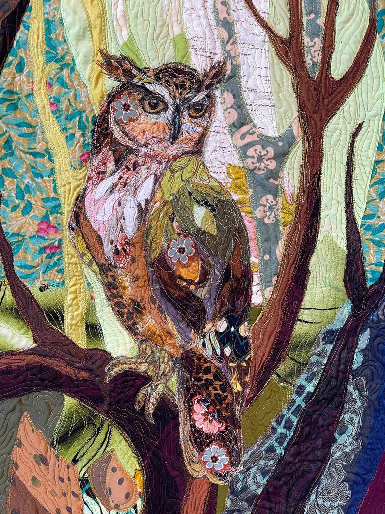 Close-up of the owl showing detailed fabric feathers, expressive eyes, floral accents, and layered textile textures.