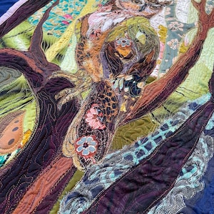 Close-up of the owl showing detailed fabric feathers, expressive eyes, floral accents, and layered textile textures.