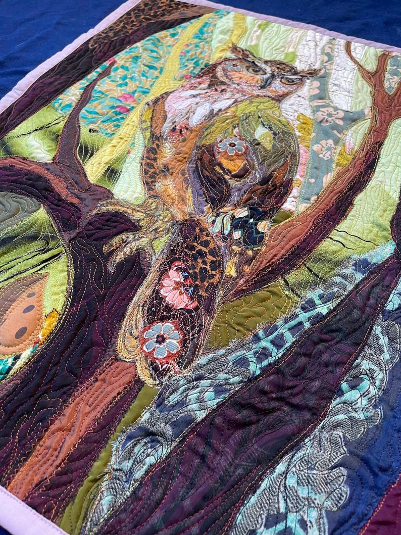 Close-up of the owl showing detailed fabric feathers, expressive eyes, floral accents, and layered textile textures.