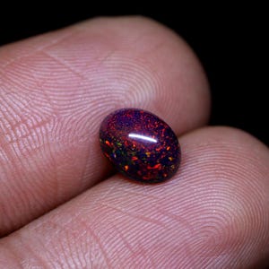 May include: A dark red, black, and green oval-shaped opal gemstone.