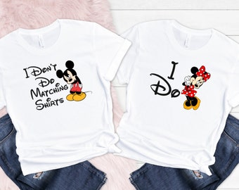 May include: Two white t-shirts with a Mickey Mouse and Minnie Mouse design. The shirt on the left says "I Don't Do Matching Shirts" and the shirt on the right says "I Do".
